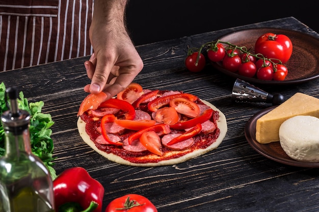 Cuocere in cucina mettendo gli ingredienti sulla pizza su un vecchio fondo di legno. Concetto di pizza. Produzione e consegna di cibo. Concetto di cucina. Avvicinamento