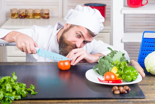 Cuocere tagliare il pomodoro cucinare il taglio e tagliare a pezzi lo chef barbuto bello in ingredienti uniformi