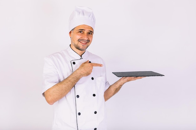 Cuoco chef che indossa giacca da cucina e cappello con in mano un vassoio di legno su sfondo bianco