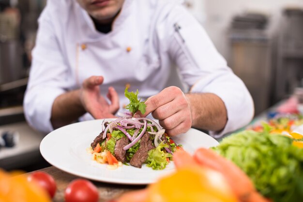 cuoco chef decorare guarnire piatto pasto preparato sul piatto nella cucina commerciale del ristorante