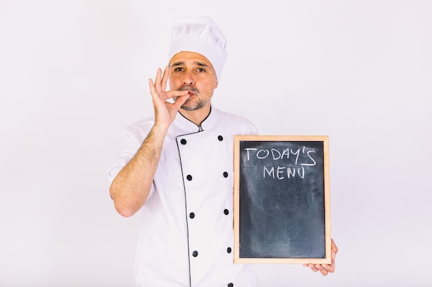 Cuoco chef in giacca e cappello da cucina sorridente, con in mano una tavola con il menu, su sfondo bianco