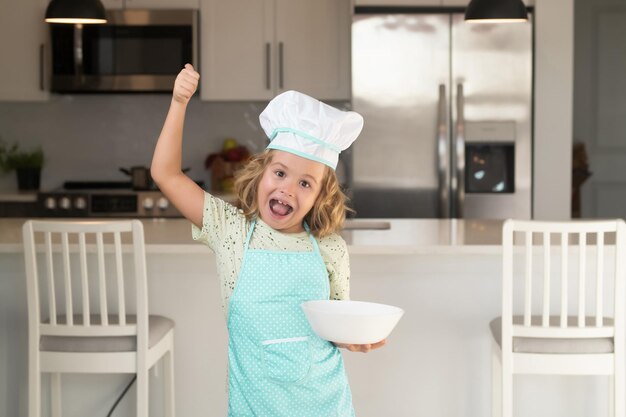 Cuoco cuoco bambino con piastra di cottura Cuoco cuoco bambino prepara il cibo in cucina Cucina per bambini Ragazzo adolescente con grembiule e cappello da cuoco che prepara un pasto sano