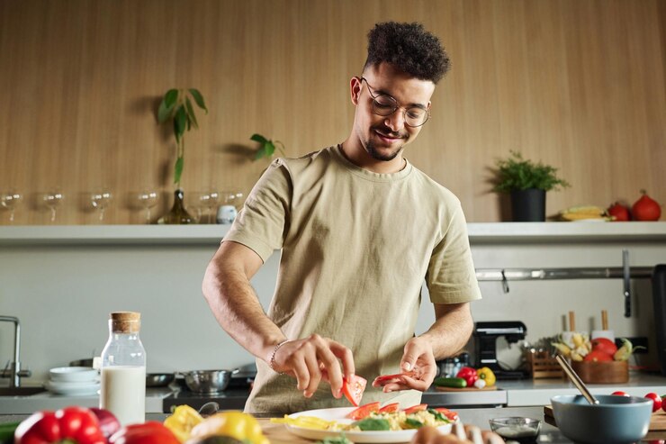 Foto cuoco del medio oriente che mette fette di pomodoro sul piatto con le verdure mentre è in piedi in cucina
