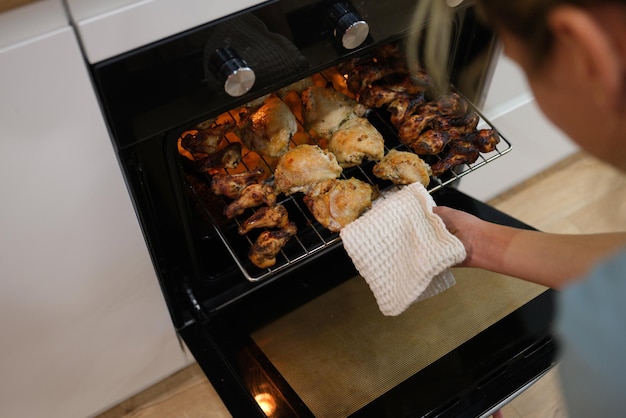 Cuoco della donna che tira fuori il pollo al forno dal forno sul primo piano della teglia