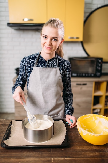 Cuoco della donna in grembiule prepara gli ingredienti della torta nella padella con carta pergamena.