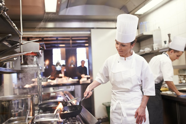 Cuoco donna e frittura nel servizio di catering della cucina del ristorante e preparazione del cibo per una cucina raffinata Cucina professionale e persona di sesso femminile soffriggere la carne con la padella per cucinare la nutrizione del pasto per l'ospitalità