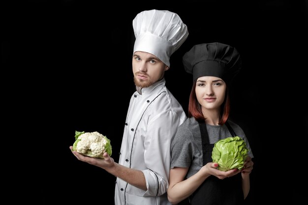 Cuoco donna in uniforme nera e chef uomo in uniforme bianca tengono cavolo verde fresco e cavolfiore o...