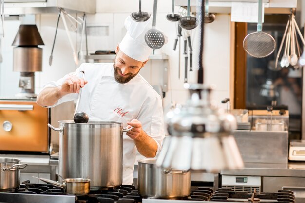 Cuoco in uniforme che cucina la zuppa nel grande fornello della cucina del ristorante