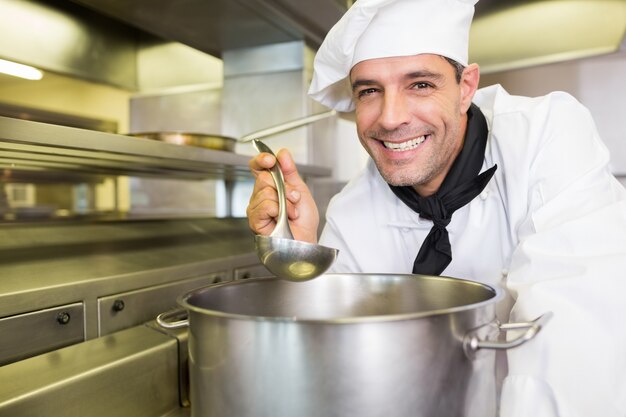 Cuoco maschio sorridente che assaggia alimento in cucina