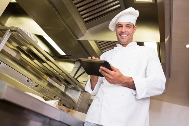 Cuoco maschio sorridente che utilizza compressa digitale nella cucina