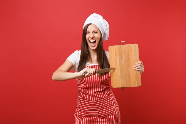 Cuoco o fornaio femminile della casalinga in grembiule a strisce, maglietta bianca, cappello del cuoco unico di toque isolato sul fondo rosso della parete. Donna della governante che tiene tagliere di legno, coltello. Deridere il concetto dello spazio della copia.