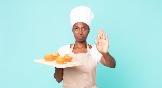 Cuoco unico adulto afroamericano nero che tiene in mano un vassoio di muffin