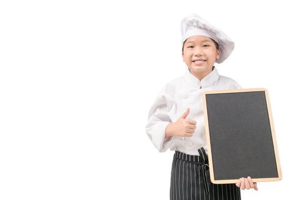 Cuoco unico asiatico felice della ragazza in uniforme che tiene lavagna in bianco isolata sulla parete bianca, per testo o menu di input con il concetto dello spazio della copia