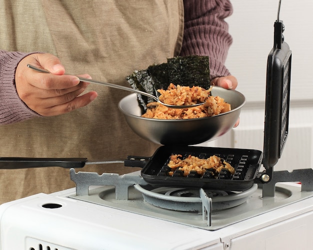 Cuoco unico asiatico femminile che fa il riso fritto di kimchi della cialda (Kimchi Bokkeumbap) o cialda di Nasi Goreng, riso virale alla moda pressato usando la macchina per waflle, popolare in Corea del sud