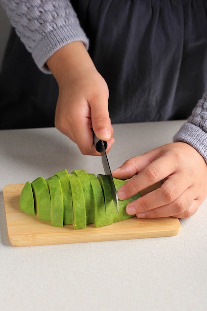 Cuoco unico asiatico per affettare a mano l'avocado su tavola di legno, primo piano, messa a fuoco selezionata