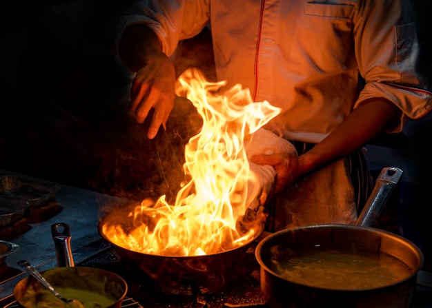 Cuoco unico che cucina con la fiamma in una padella su una stufa di cucina