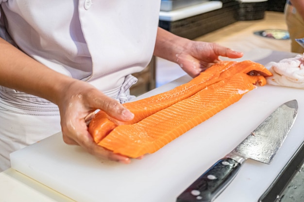 Cuoco unico che prepara e che taglia salmone fresco in ristorante giapponese