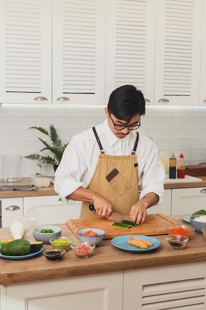 Cuoco unico che prepara il cuoco unico asiatico dei sushi in ingredienti per affettare uniformi sulla cucina bianca
