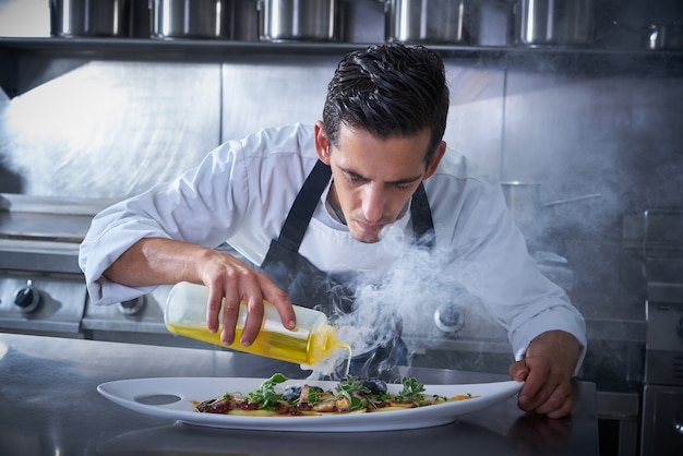 Cuoco unico che prepara il polipo in cucina con il fumo