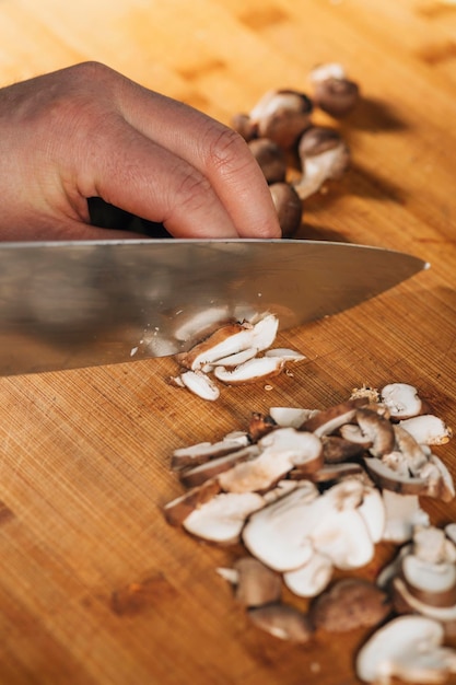 Cuoco unico che taglia i funghi Shiitake con il coltello su un tagliere di legno