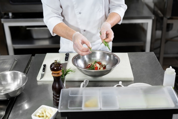 Cuoco unico dell'uomo bello che prepara il piatto con i gamberetti al tavolo in cucina