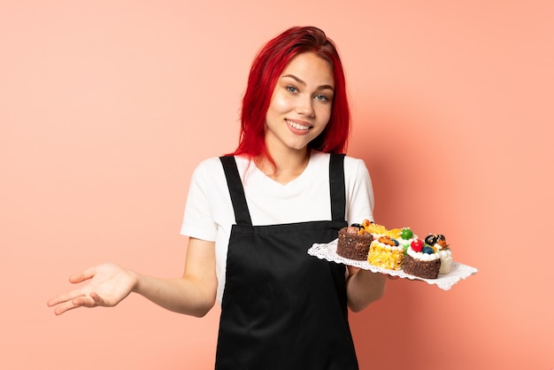 Cuoco unico di pasticceria che tiene muffin sulla parete rosa felice e sorridente