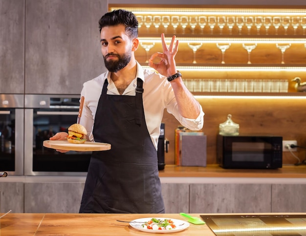 Cuoco unico felice del ritratto con i pasti cucinati per una cena nello spazio della copia della cucina e nello spazio vuoto f