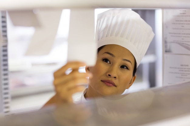 Cuoco unico femminile che passa la lista di controllo di cottura alla cucina