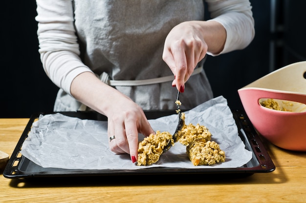 Cuoco unico femminile che prepara i biscotti di farina d&#39;avena, stende l&#39;impasto sui vassoi.