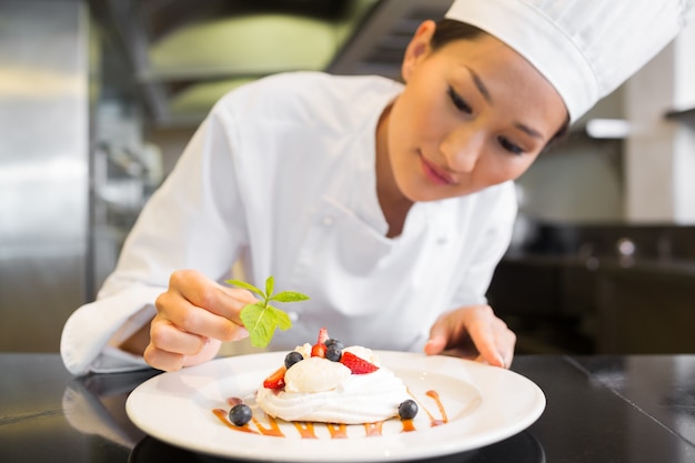 Cuoco unico femminile concentrato che guarnisce alimento in cucina