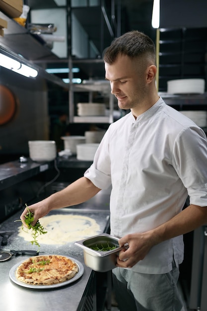 Cuoco unico maschio che cosparge di verde fresco sopra la pizza fatta tradizionalmente. Ristorante fast food italiano