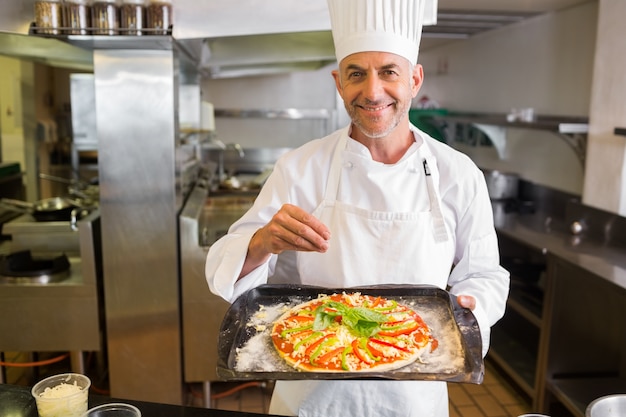 Cuoco unico maschio sicuro che tiene alimento cucinato in cucina