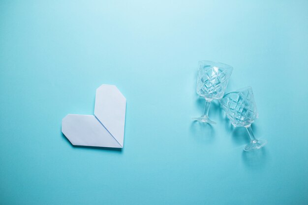 Cuore bianco di origami con i vetri di vino su fondo blu. Carta di San Valentino su sfondo blu.