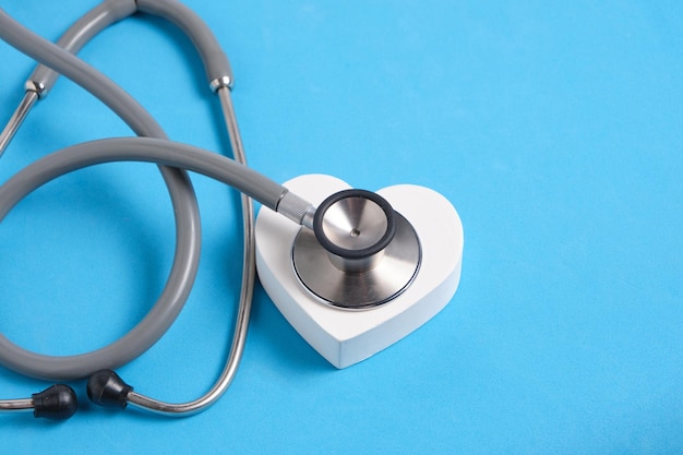 Cuore bianco e stetoscopio su sfondo blu Visita medica per malattie cardiache