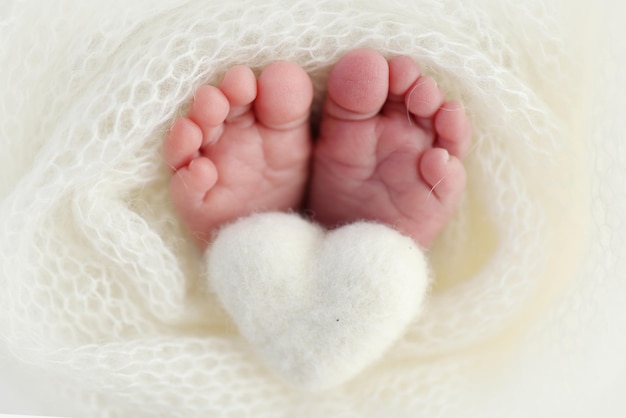 Cuore bianco lavorato a maglia nelle gambe di un bambino Macrofotografia Il minuscolo piede di un neonato Piedi morbidi di un neonato in una coperta di lana bianca Primo piano dei talloni e dei piedi di un neonato