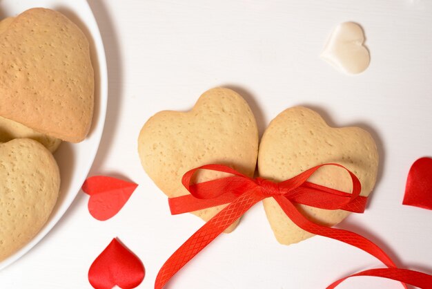 Cuore del biscotto legato con il nastro rosso per il giorno di San Valentino, primo piano, cottura per le vacanze. vista dall'alto di cuori decorativi.