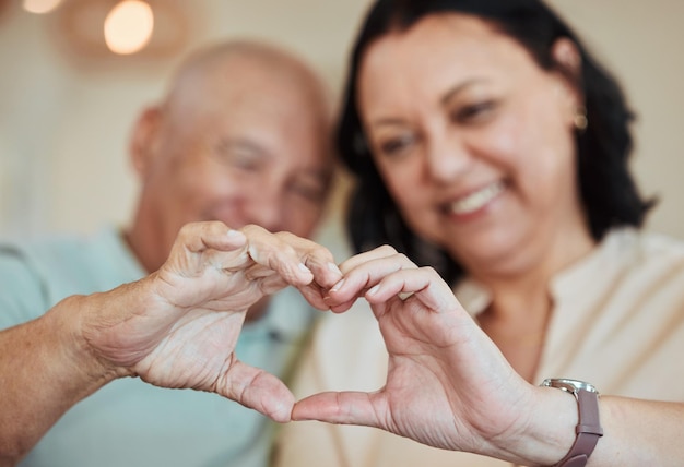 Cuore delle mani e amore con una coppia anziana nella loro casa per la salute, il benessere o la fiducia durante la pensione Forma Emoji o gesto della mano con un uomo anziano e una donna in primo piano nella loro casa insieme