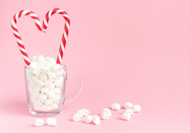 Cuore di bastoncini di zucchero bianco e marshmallow in tazza su sfondo rosa Concetto felice giorno di San Valentino