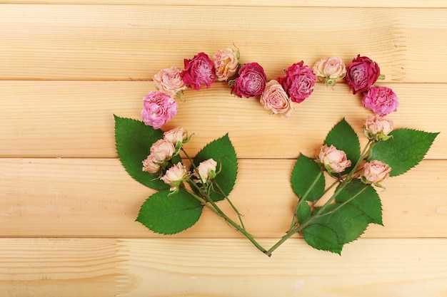 Cuore di bei fiori secchi e foglie verdi su fondo di legno