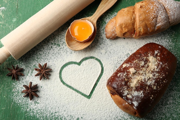 Cuore di farina, croissant e utensili da cucina in legno su sfondo verde