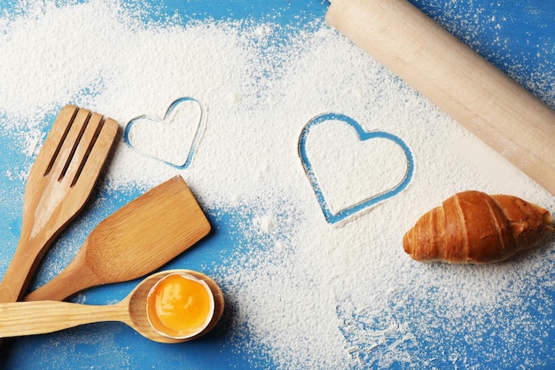 Cuore di farina e utensili da cucina in legno su sfondo blu