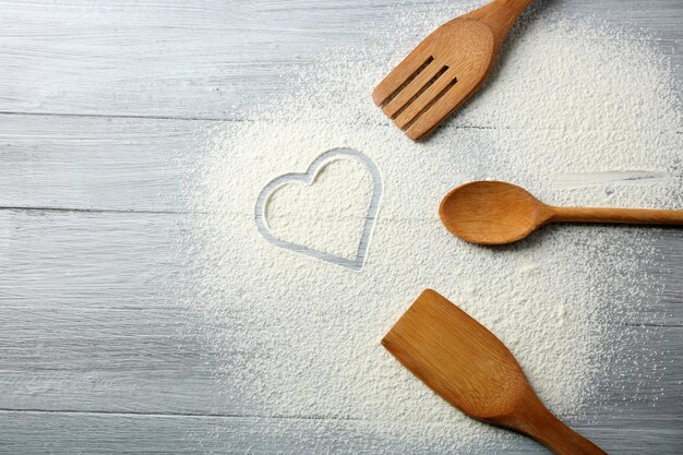 Cuore di farina e utensili da cucina su fondo di legno