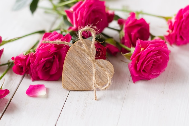 Cuore di legno e rose rosa sulla tavola bianca di legno per il giorno di S. Valentino