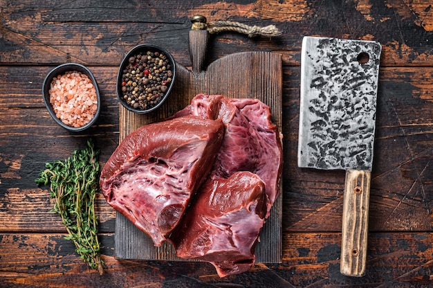 Cuore di manzo o vitello affettato crudo su un tagliere con mannaia di carne. Tavolo in legno scuro. Vista dall'alto.