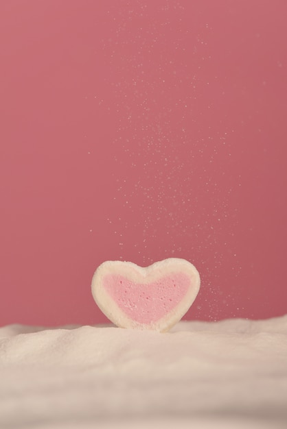 Cuore di marshmallow su uno sfondo rosa in zucchero a velo.