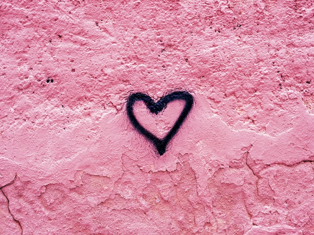 Cuore disegnato con vernice spray nera su una parete rosa danneggiata