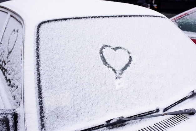 Cuore disegnato sul parabrezza di un'auto coperto di neve fresca di Natale