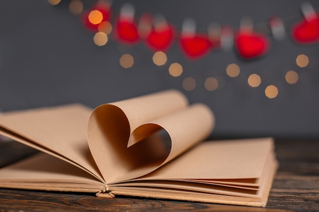 Cuore fatto da fogli di libri in luci, amore e concetto di San Valentino su un tavolo di legno