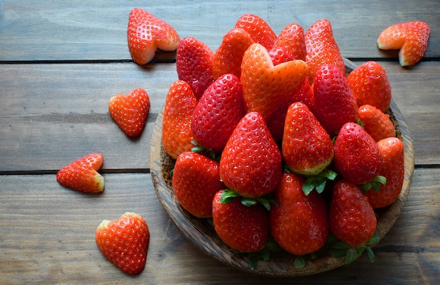 Cuore fresco della fragola e della fragola in piatto di legno su fondo di legno