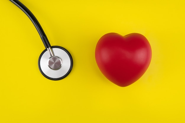 Cuore giocattolo e uno stetoscopio su sfondo giallo. Vista dall'alto. Sanità di concetto. Cardiologia - cura del cuore